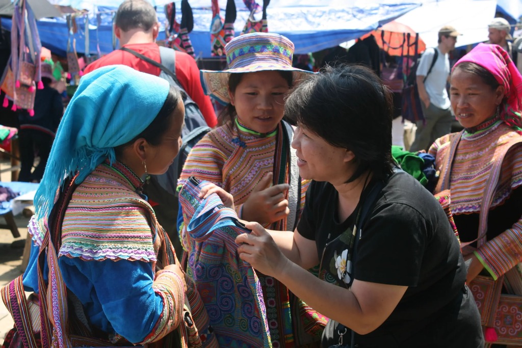 A shopper bargaining over embroidered textiles with Hmong women at a highland market
