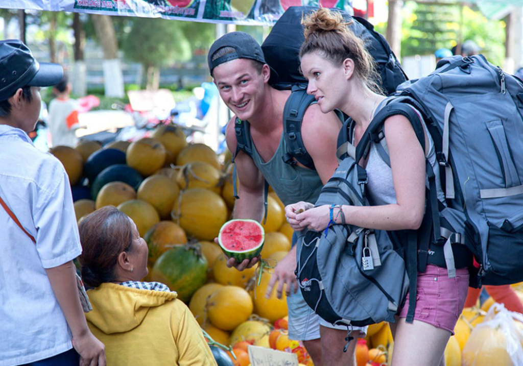 Two backpackers buying watermelon and melons from a street fruit seller