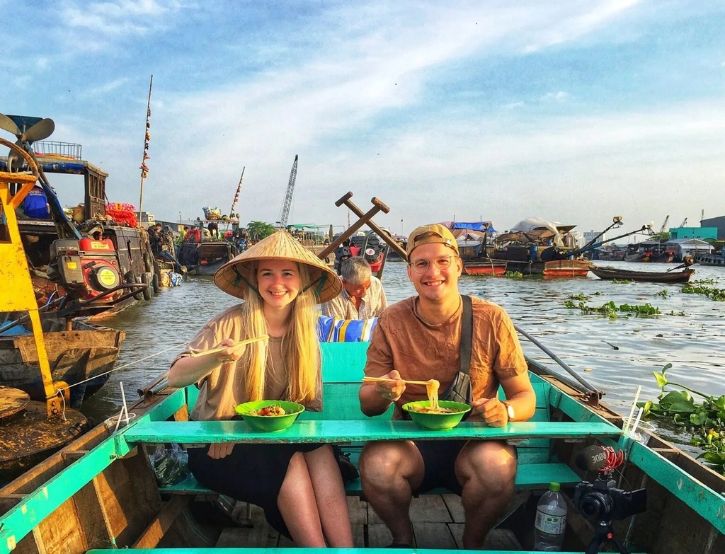 Two travellers eating noodles on a boat at a floating market in the Mekong Delta